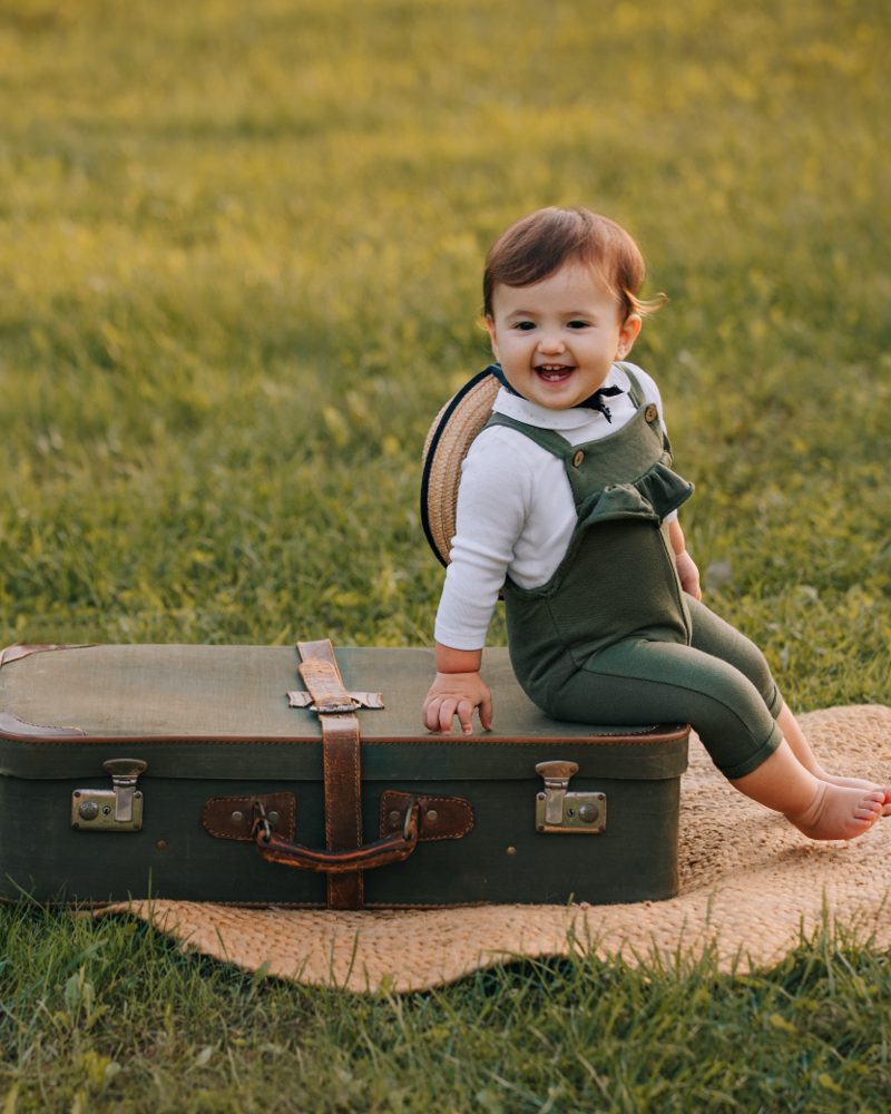 Bambina sorridente seduta su una valigetta d'epoca in un prato durante un servizio fotografico all'aperto