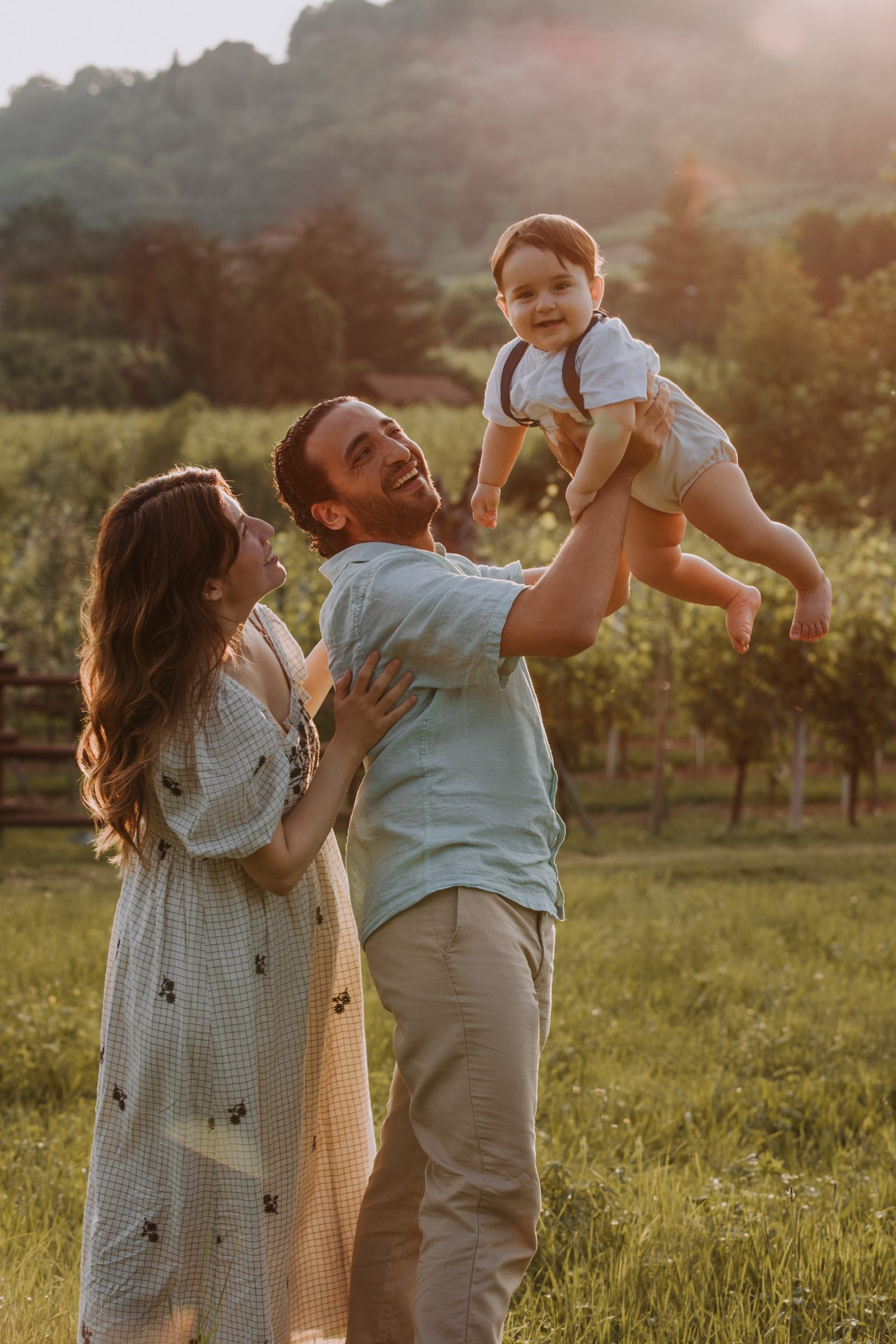 Papà che alza in braccio il suo bambino al tramonto tra i cipressi